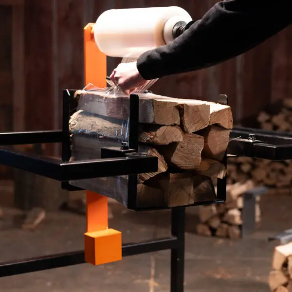 Close-up of a worker cutting shrink wrap on a tightly bound firewood bundle created with the IronEmber Firewood Bundler, preparing it for use.